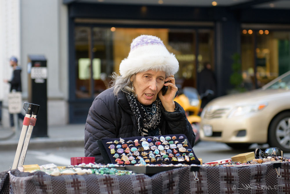 _JMS0041.jpg - This is an expensive city, and many residents supplement their income by busking or doing a little sidewalk vending.  This woman is one example.  She seemed the very picture of a sweet little old lady until she saw me taking her picture.  Then I found her vocabulary and demeanor to more closely resemble that of a dock worker.  She chased me down the street shouting obscenities and demanding that I give her my camera.  I have to wonder if she was lacking some sort of license.