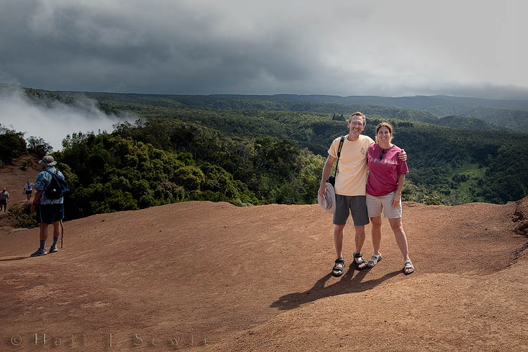 2009_09_28_Hawaii-244-Edit.jpg - It was a beautiful morning when we left Lihue to drive to Waimea, but by the time we got to the canyon the morning clouds had settled down into the valley but we still headed up into the mountains to see what there was to see.  When we reached Puu o Kila Lookout it was pouring rain. As we sat in the car watching people hurry back from the Kalalau valley trail the rain cleared and the sun came out so we took a short walk along the beginning (or end) of the trail until it started to rain again, about 20 minutes later. You can see how the clouds and fog came up from the valley behind us.  One moment you could see out over the valley and then 30 seconds later it would be completely covered in clouds. We traded favors of pictures with another family to get this shot of the two of us.