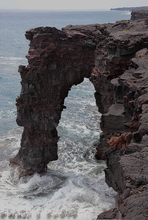 2009_10_02_Hawaii-10253.jpg - At the end of the Chain of Craters road, just before where the new lava flow bisected the road is the Holei Sea Arch.  Sea arches are not unusual, what is unusual is being able to see one so well.  The arch is formed because of the power of the water pounding the lava and wearing it down, the "softest" rock being worn away first.  To get this picture Mike held onto me as I leaned over the the wall of the 80 foot high cliff.  Really!