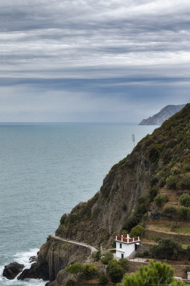 2017_09_15_Italy-10233-Edit1000.jpg - Our home base for the 6 days we spent in Cinque Terre was Riomaggiore.  We stayed in another wonderful Airbnb and although we couldn't hike between the towns we bought a rail pass and spent a day in each one of the 5 towns that make up the Cinque Terre.  This shot shows the Via dell'Amore, or the Way of Love, as it winds around the cliff from Riomaggiore to Manarola.  Unfortunately due to rock falls and jurisdictional disputes the Via dell'Amore has been closed for a while and the paths higher up through the hills have become over-used prompting some land owners to request they be closed as well.
