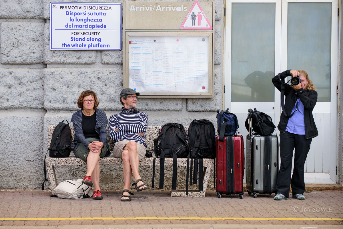 _JMS2869.jpg - This is not a great picture, but it relays a funny message. We're waiting for our train to take us back to Florence, and killing time by playing with our cameras.  Not everyone will smile when they suspect they might be in a picture. But some people get nasty about it.  As made evident by the stink-eye we received from the striped duo on the bench at the train station. I laugh every time I look at this shot.