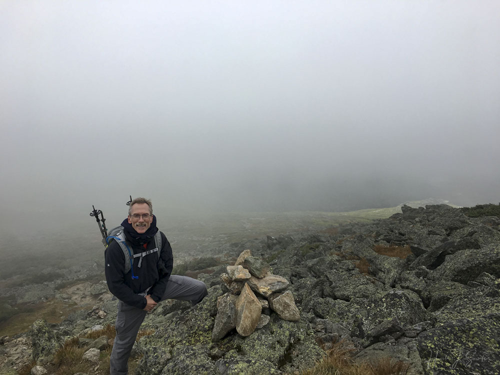 2018_09_WhiteMountainsNH-10247-Edit1000.jpg - Mike at a cairn at the summit.  It was still pretty fogged in despite the wind.